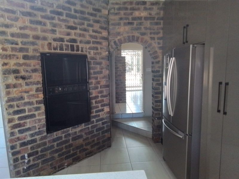 Kitchen area featuring exposed brick walls, built-in oven, and tiled flooring, leading through an arched doorway to an adjacent space.