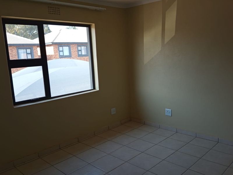 A clean, empty bedroom featuring neutral wall paint, tiled flooring, and a large aluminium-framed window providing natural light.