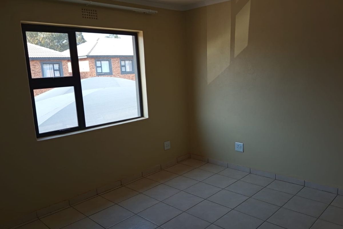 A clean, empty bedroom featuring neutral wall paint, tiled flooring, and a large aluminium-framed window providing natural light.