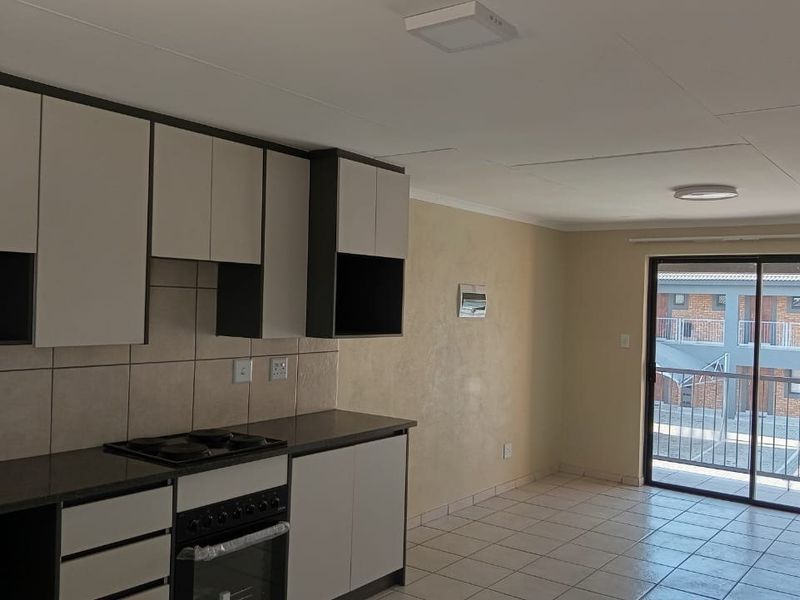 Open-plan kitchen and living area featuring tiled floors, modern cabinetry with built-in oven and hob, and access to a private balcony.