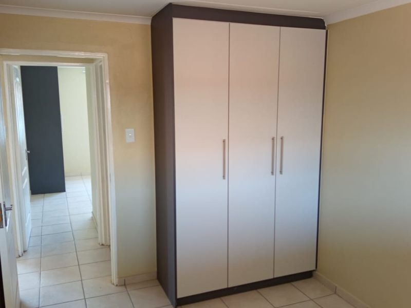 A clean, empty bedroom featuring neutral wall tones, tiled flooring, and a modern built-in wardrobe with sleek handles.
