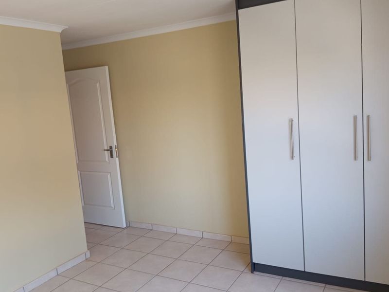 A clean, empty bedroom featuring neutral wall paint, tiled flooring, and a modern built-in wardrobe with white doors.