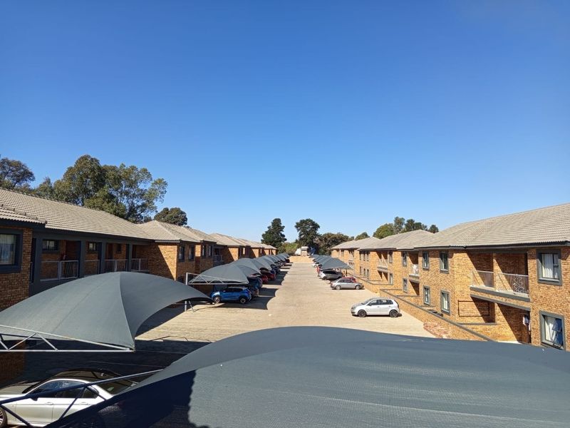 An elevated view of the apartment complex grounds featuring paved driveways, covered parking bays with shade cloth, and brick building exteriors.