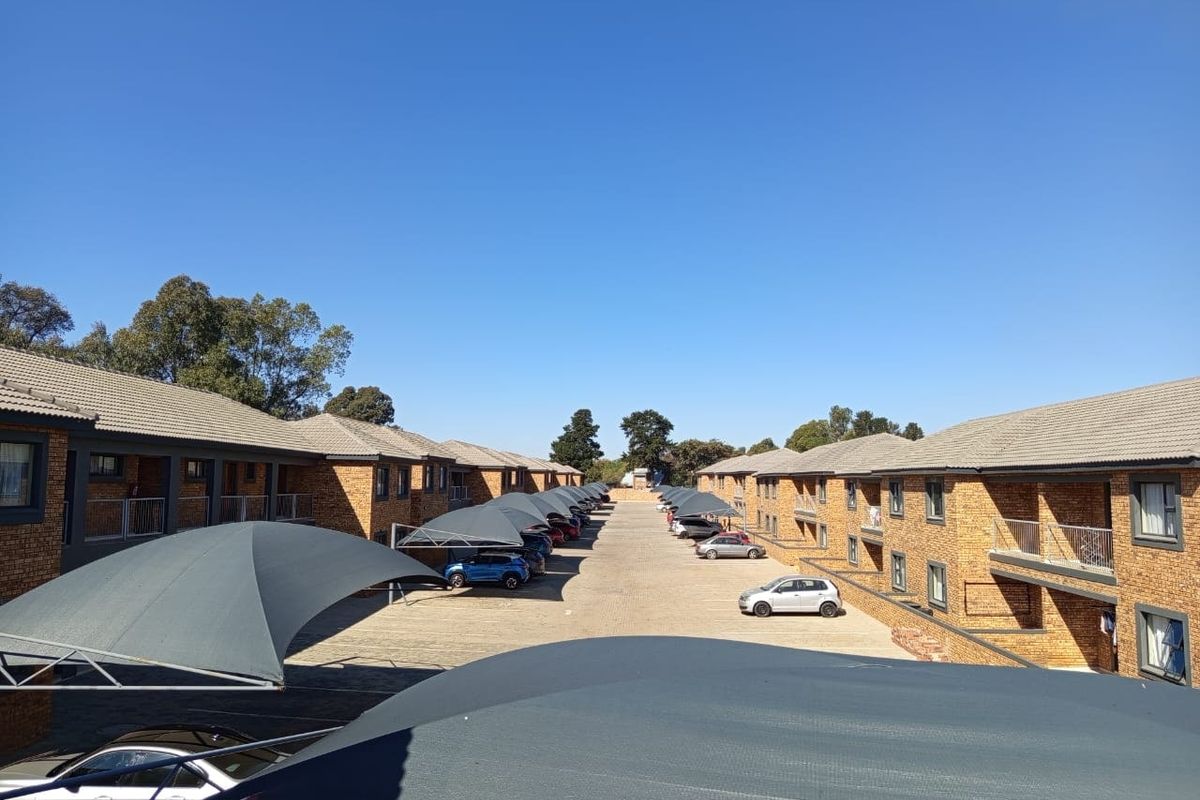 An elevated view of the apartment complex grounds featuring paved driveways, covered parking bays with shade cloth, and brick building exteriors.