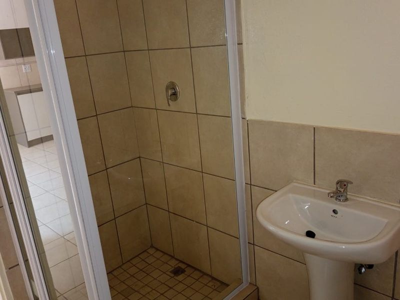 A functional bathroom featuring a pedestal washbasin and a glass-enclosed shower with neutral ceramic wall and floor tiling.