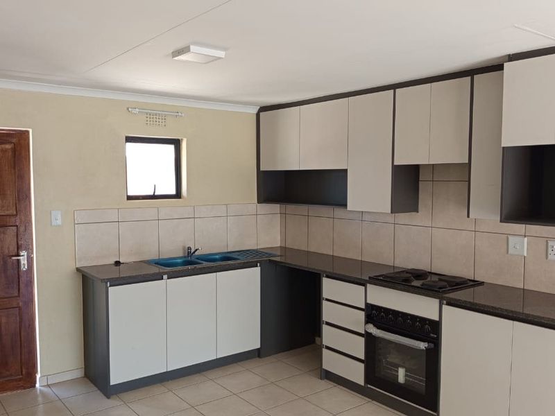 A clean, functional kitchen featuring modern two-tone cabinetry, granite countertops, a built-in oven and hob, and neutral tiled flooring.