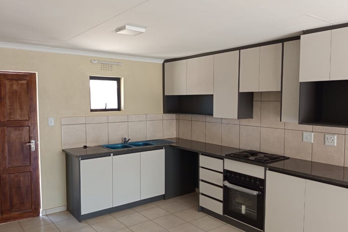 A clean, functional kitchen featuring modern two-tone cabinetry, granite countertops, a built-in oven and hob, and neutral tiled flooring.
