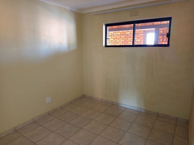An empty bedroom featuring tiled flooring, a sliding window, and neutral wall finishes, providing a blank canvas for personalization.