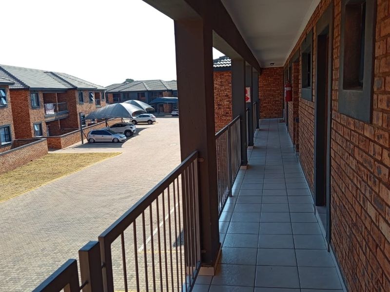 An exterior apartment hallway featuring tiled flooring, exposed brick walls, and a metal balustrade overlooking the complex parking area.