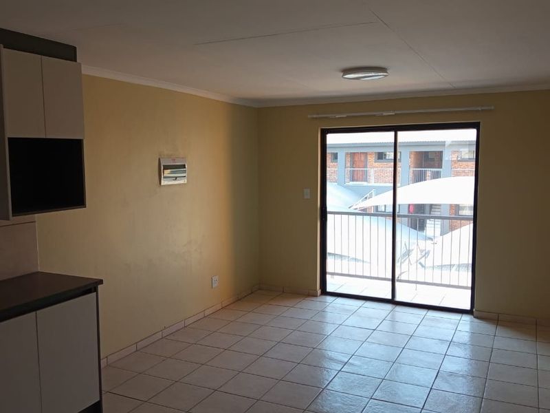 An open-plan living and kitchen area featuring tiled flooring, neutral walls, and a sliding glass door leading to a balcony.