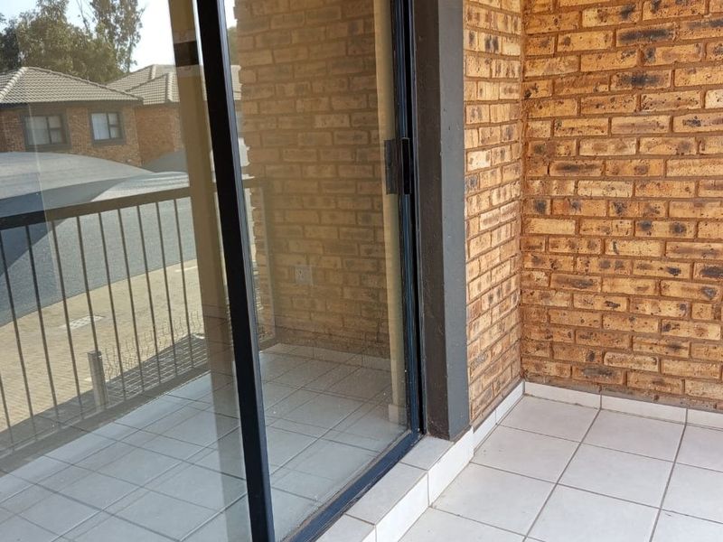 A private balcony featuring exposed brick walls, tiled flooring, and a metal balustrade, accessible via a sliding glass door.