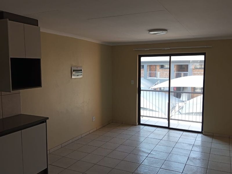Open-plan living area featuring tiled flooring, built-in kitchen cabinetry, and a sliding glass door leading to a balcony.