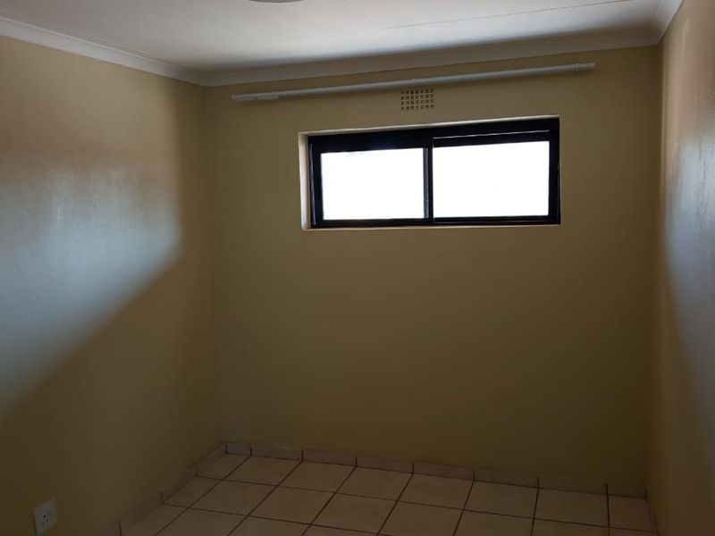 An empty bedroom featuring tiled flooring, neutral wall paint, and a sliding window with a curtain rod.