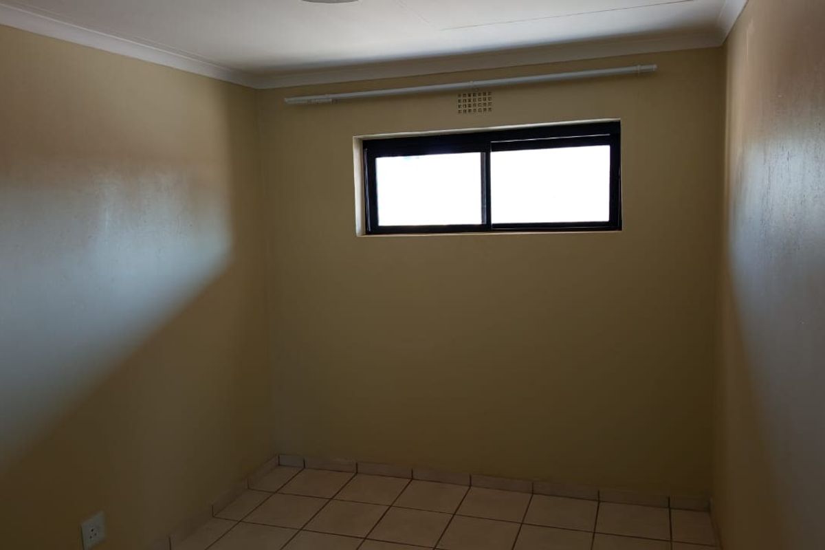 An empty bedroom featuring tiled flooring, neutral wall paint, and a sliding window with a curtain rod.