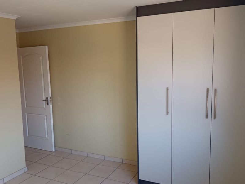 A clean, empty bedroom featuring neutral wall tones, tiled flooring, and a functional built-in wardrobe with modern handles.