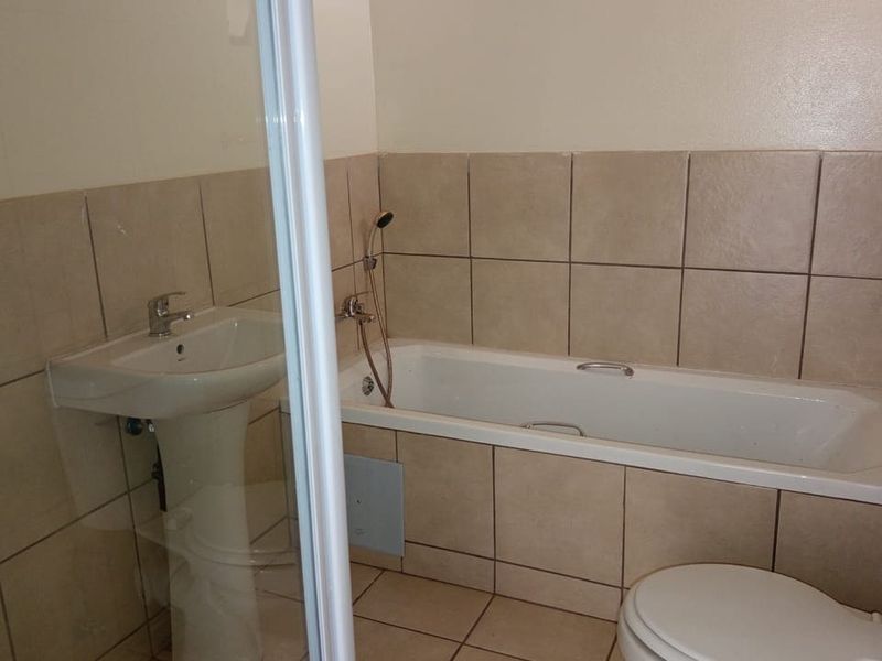 A functional bathroom featuring a pedestal basin, bathtub, separate shower enclosure, and toilet with neutral ceramic tiling throughout.
