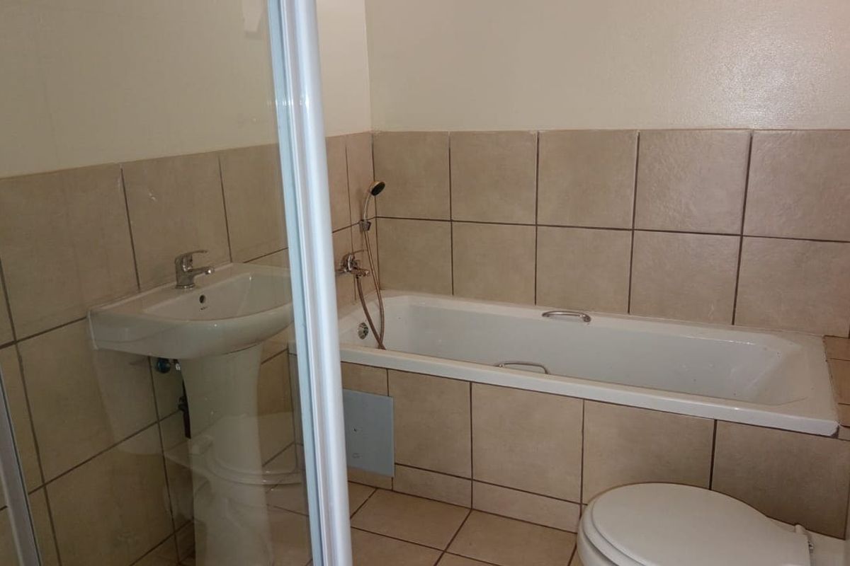 A functional bathroom featuring a pedestal basin, bathtub, separate shower enclosure, and toilet with neutral ceramic tiling throughout.