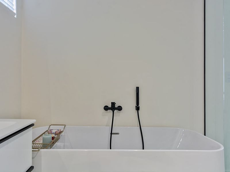 Modern bathroom featuring a sleek white freestanding bathtub with contemporary matte black wall-mounted fixtures and a glass shower screen.