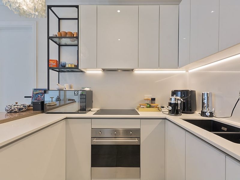 Modern U-shaped kitchen featuring sleek white cabinetry, stone countertops, integrated appliances, and contemporary under-cabinet lighting.
