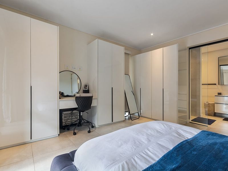 Modern bedroom featuring extensive built-in white cabinetry, tiled flooring, and an integrated en-suite bathroom separated by a sleek glass partition.
