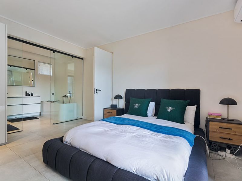 Modern bedroom featuring tiled flooring, an integrated air conditioning unit, and a contemporary en-suite bathroom separated by a sleek glass partition wall.