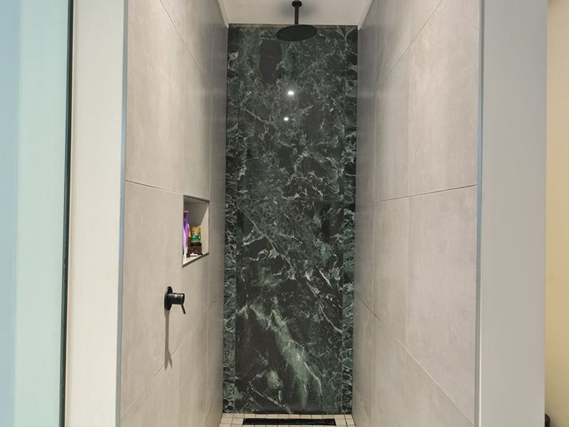 A modern walk-in shower featuring a striking green marble accent wall, matte black fixtures, and a convenient built-in recessed storage niche.