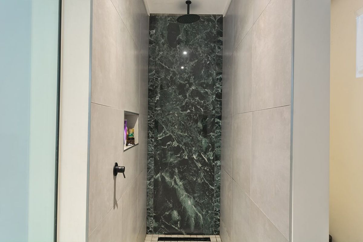 A modern walk-in shower featuring a striking green marble accent wall, matte black fixtures, and a convenient built-in recessed storage niche.