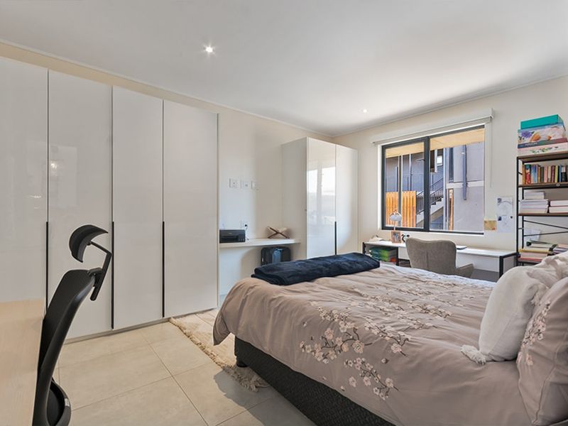 A well-maintained bedroom featuring modern built-in cupboards, tiled flooring, and large aluminium-framed windows providing natural light.
