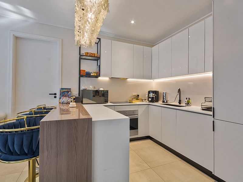 Modern kitchen featuring sleek white cabinetry, stone countertops, integrated appliances, and a functional breakfast bar island with contemporary lighting.