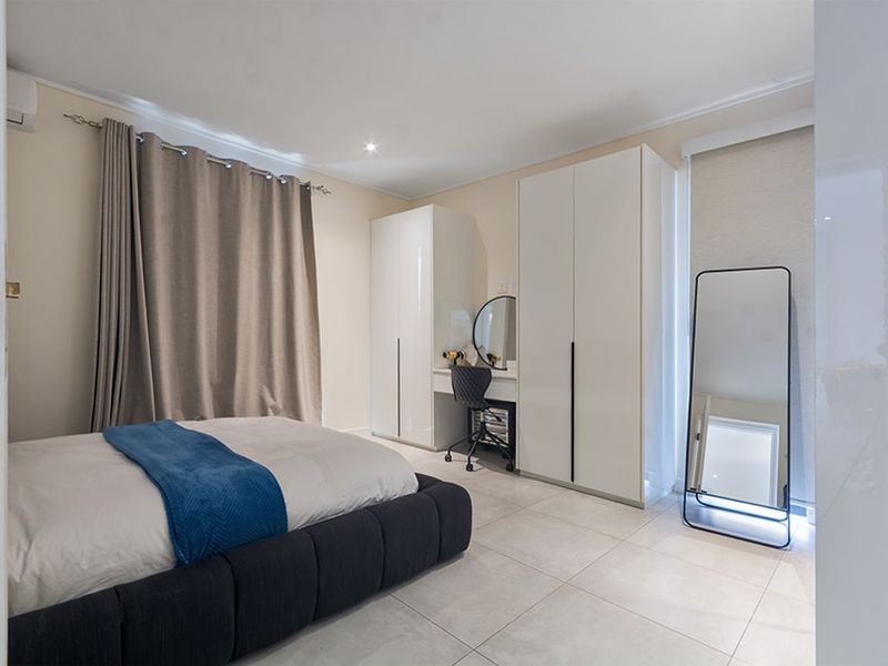A well-maintained bedroom featuring neutral tiled flooring, built-in high-gloss cabinetry, and an integrated air conditioning unit.