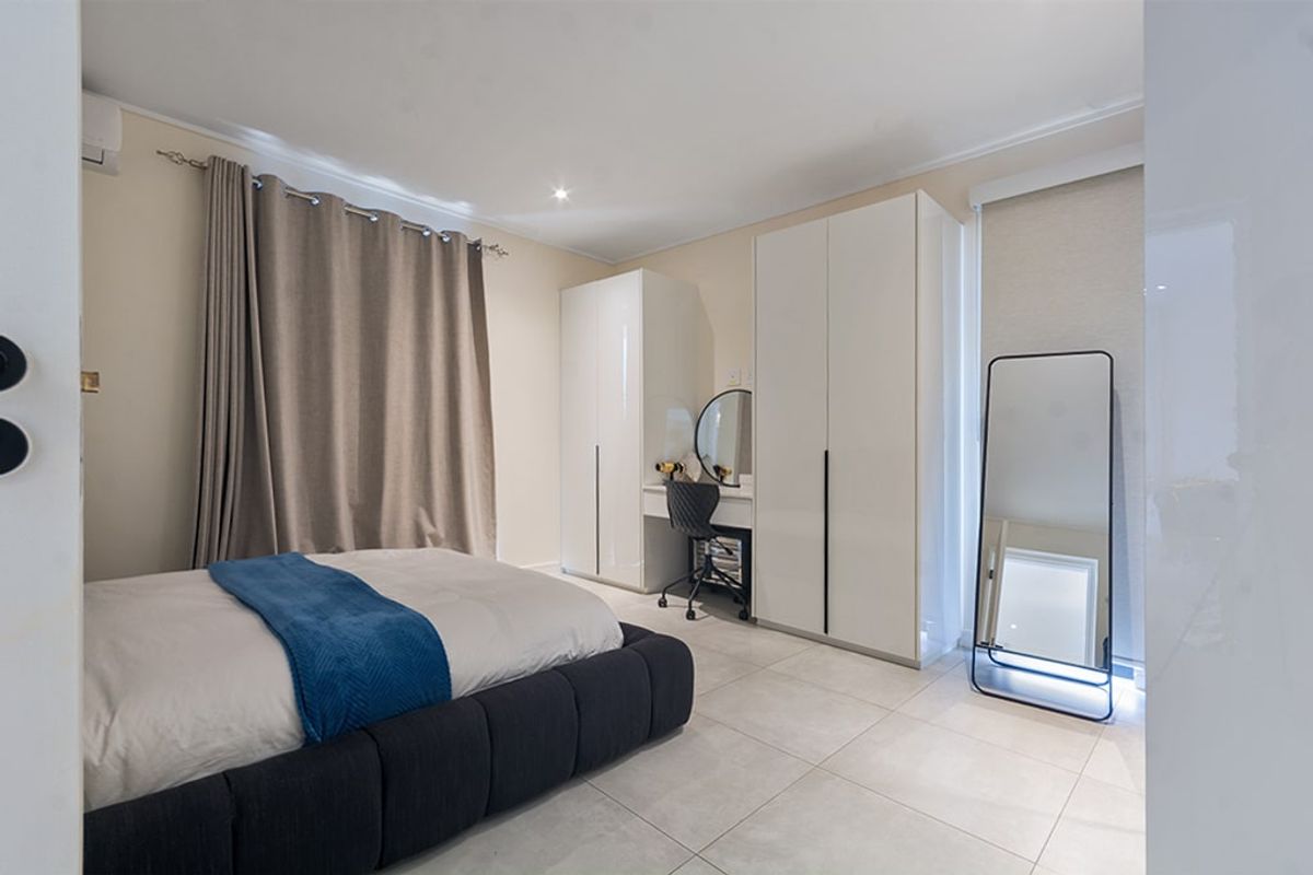 A well-maintained bedroom featuring neutral tiled flooring, built-in high-gloss cabinetry, and an integrated air conditioning unit.