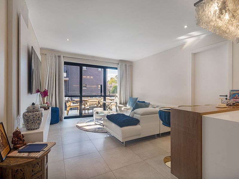 Modern open-plan living area featuring tiled floors, recessed lighting, and seamless access to an outdoor balcony through large sliding glass doors.