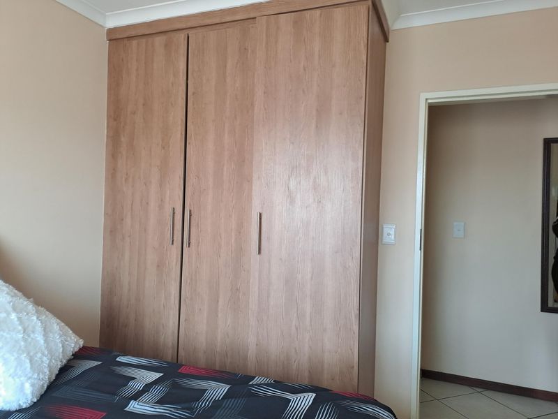 A bedroom featuring a large, wood-finish built-in wardrobe with modern handles and neutral wall tones.