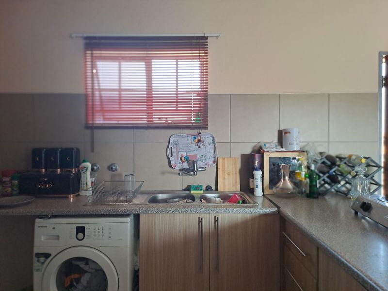 A functional kitchen area featuring laminate countertops, a double sink, tiled backsplash, and integrated space for a washing machine.