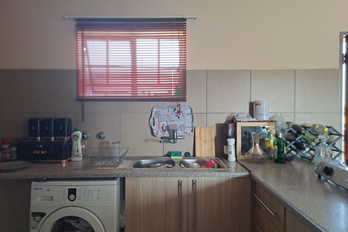 A functional kitchen area featuring laminate countertops, a double sink, tiled backsplash, and integrated space for a washing machine.