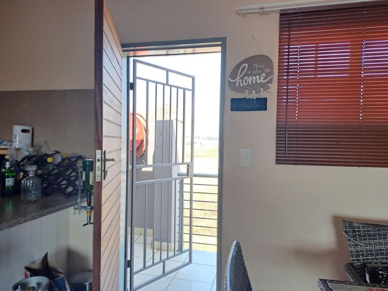 A view from an interior space through a security gate leading to an outdoor balcony area with tiled flooring and metal railings.