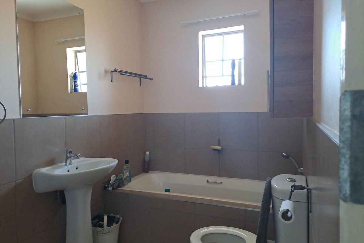 A functional bathroom featuring a pedestal basin, bathtub, toilet, and wall-mounted mirror with neutral wall tiles and cabinetry.