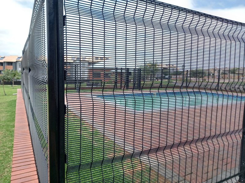 A view of a communal swimming pool area enclosed by modern black security mesh fencing with paved surrounds.