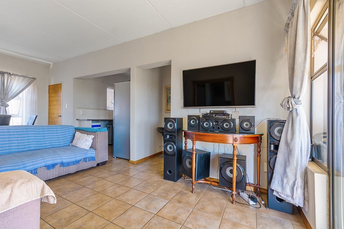 A living room featuring ceramic floor tiles, a sliding glass door, and a wall-mounted television, with an adjacent view into the kitchen area.