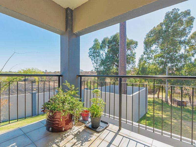 A covered balcony featuring tiled flooring and a metal balustrade, offering an open view of the surrounding garden and landscape.