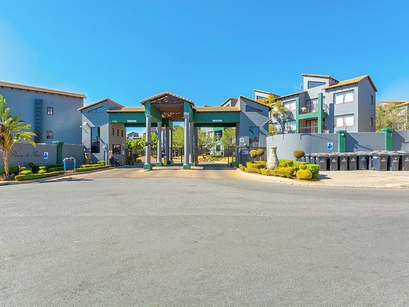 The main entrance and security gatehouse of the apartment complex, featuring a paved driveway and established perimeter walling.