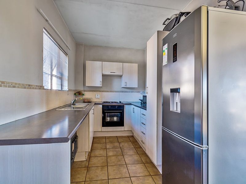 A functional kitchen featuring built-in cabinetry, laminate countertops, a tiled backsplash, and integrated cooking appliances with tiled flooring throughout.