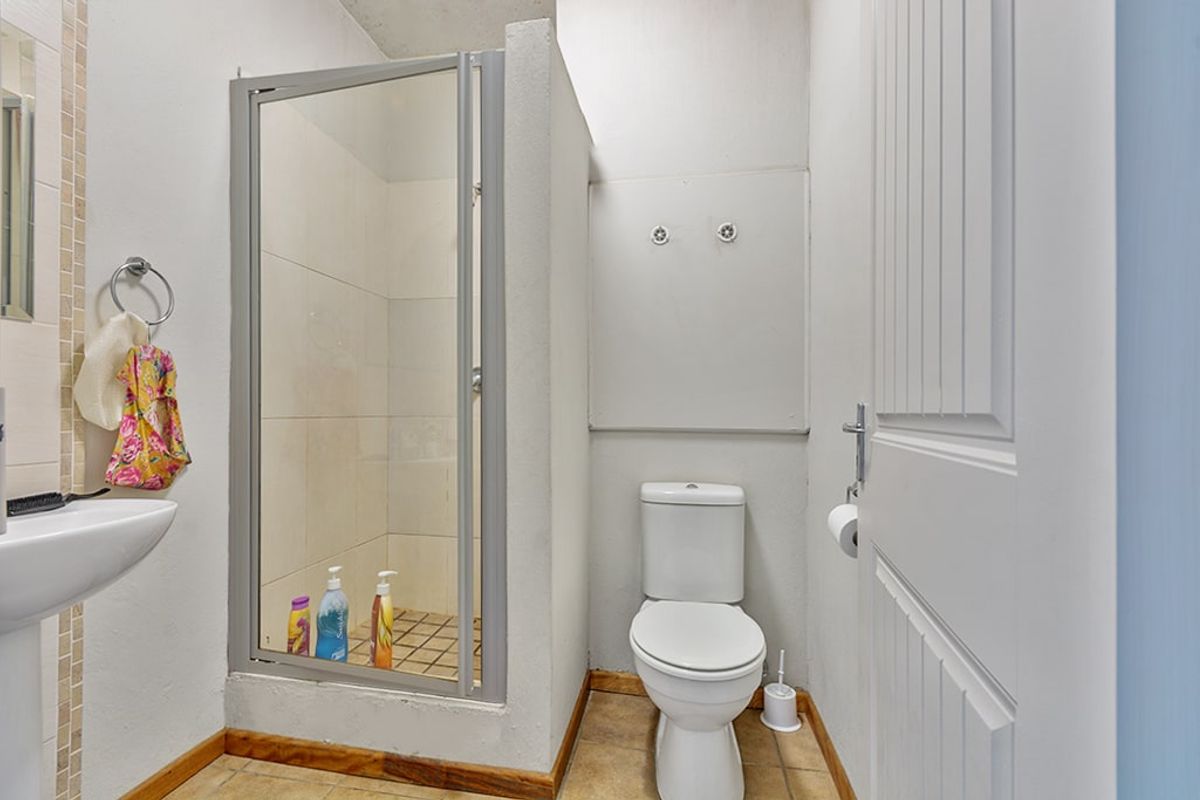 A functional bathroom featuring a shower enclosure, a standard toilet, and a wall-mounted basin with tiled flooring.