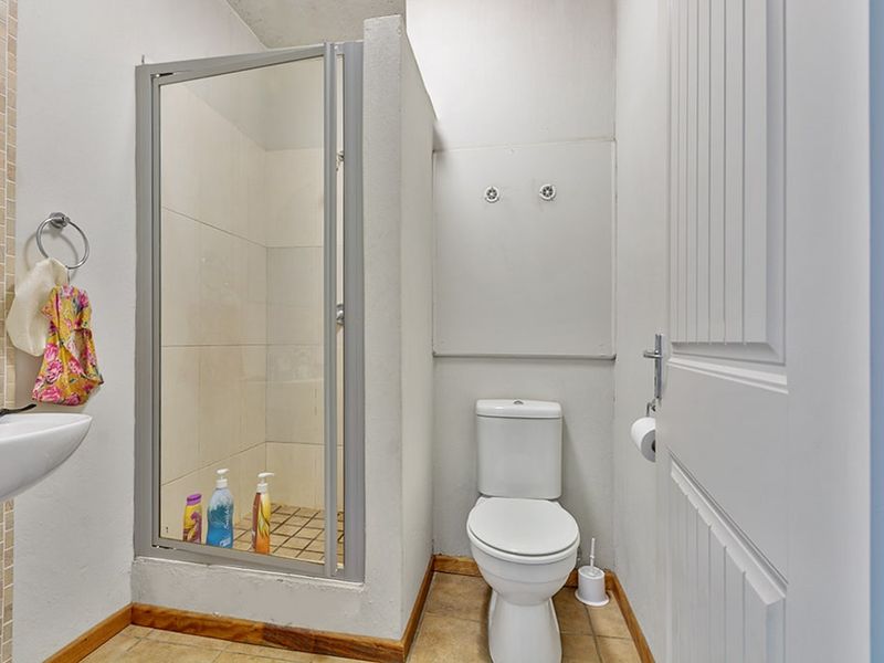 A functional bathroom featuring a shower enclosure, a standard toilet, and a wall-mounted basin with tiled flooring.