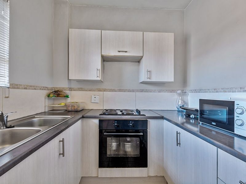 Compact kitchen featuring light wood-grain cabinetry, dark laminate countertops, a built-in oven with electric hob, and a stainless steel double sink.