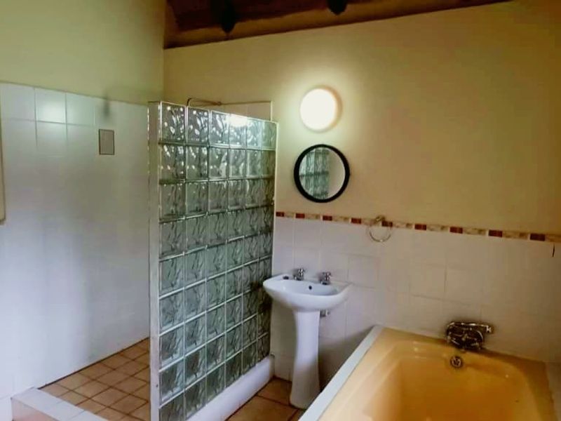 A functional bathroom featuring a glass block shower enclosure, a pedestal sink, and a vintage-style bathtub with tiled wall accents.