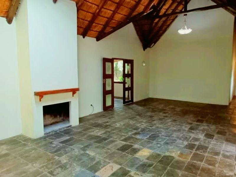 Spacious living area featuring a high vaulted thatched ceiling, exposed timber beams, a built-in fireplace, and durable slate tile flooring.