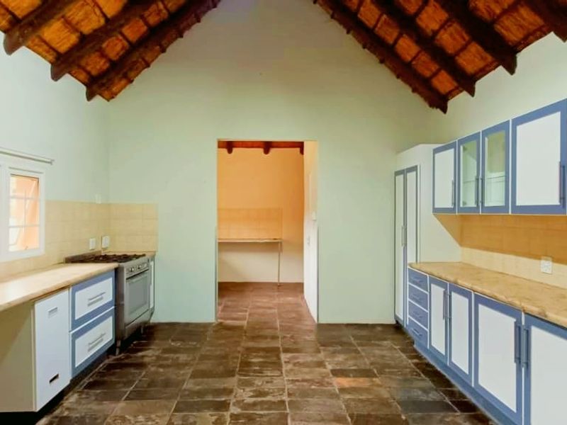 Spacious kitchen featuring a high vaulted thatched ceiling, tiled flooring, and ample built-in cabinetry with a freestanding stove and oven.