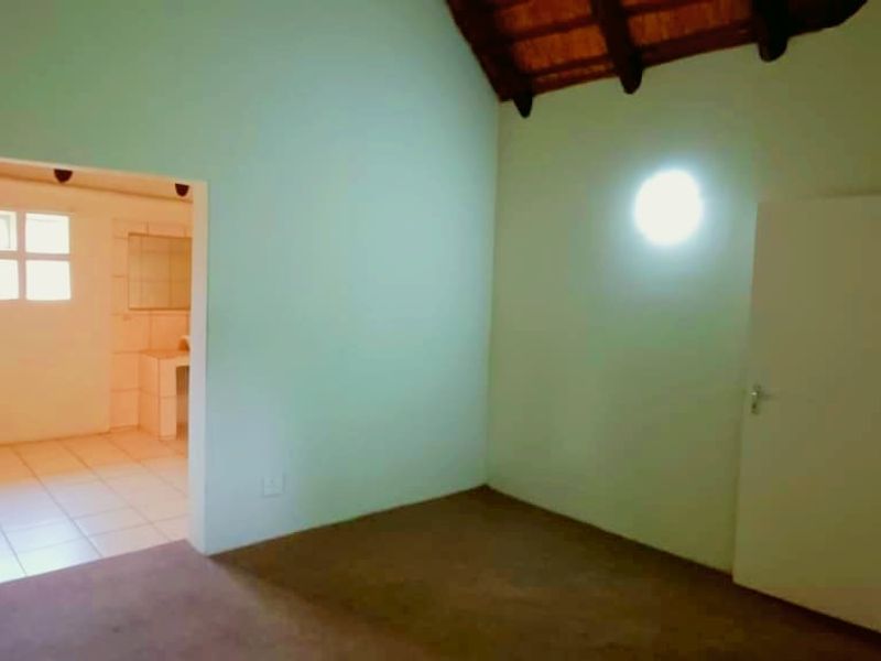 A spacious bedroom featuring high vaulted ceilings with exposed timber beams, carpeted flooring, and direct access to an adjoining bathroom.