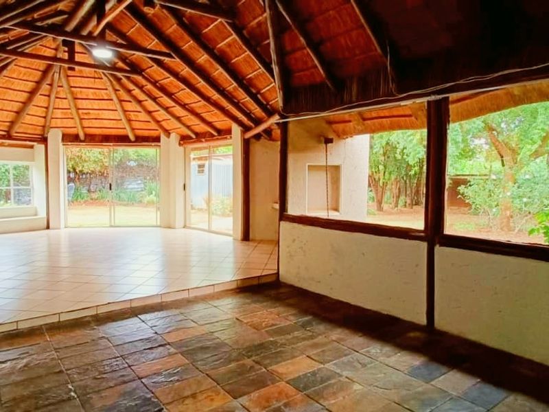 Spacious covered patio area featuring a traditional thatched roof, exposed timber beams, and large windows overlooking the garden.